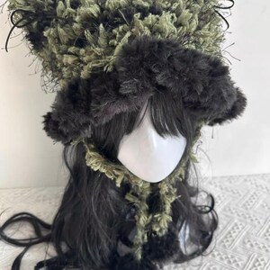 Puede incluir: Un sombrero caprichoso, hecho a mano, con un dise&ntilde;o &uacute;nico. El sombrero presenta una corona esponjosa y texturizada en tonos verdes y negros, con detalles en negro y peque&ntilde;os lazos. El ala es de un material m&aacute;s oscuro y afelpado. El sombrero forma parte de un conjunto de disfraz o cosplay.