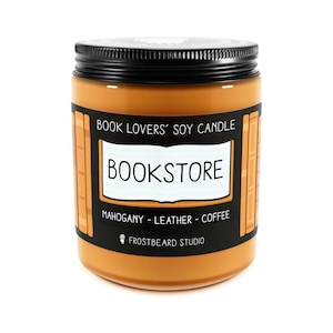 May include: A soy candle in a glass jar with a black lid. The label reads "BOOKSTORE" and "BOOK LOVERS' SOY CANDLE". The scent notes are mahogany, leather, and coffee. The candle is a warm brown color.