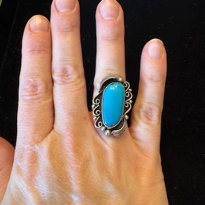 Peut inclure: Une bague en argent avec une pierre turquoise sertie dans un motif en spirale.