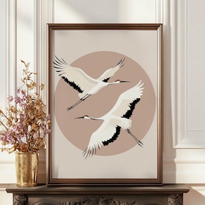 Könnte beinhalten: Gerahmter Kunstdruck mit zwei weißen Kranichen im Flug vor einem sanften, rosa kreisförmigen Hintergrund. Die Vögel haben schwarze Flügelspitzen und lange, schlanke Schnäbel. Das Kunstwerk wird in einem braunen Holzrahmen präsentiert.