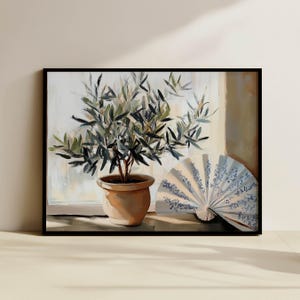 Puede incluir: Pintura enmarcada que representa un olivo en maceta junto a un abanico plegado. El abanico es blanco con motivos florales azules. El olivo tiene hojas verdes y está en una maceta de terracota. El fondo sugiere una ventana con luz suave.