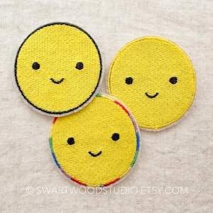 May include: Three yellow felt smiley face patches with black embroidered eyes and mouths. One patch has a rainbow border.