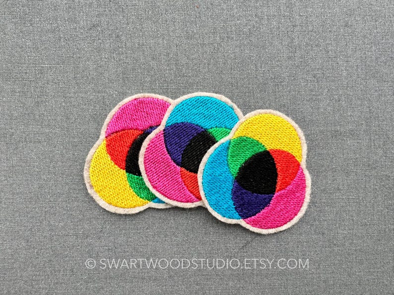 May include: Three colourful embroidered patches in the shape of overlapping circles. The patches are yellow, red, green, blue, pink and black.