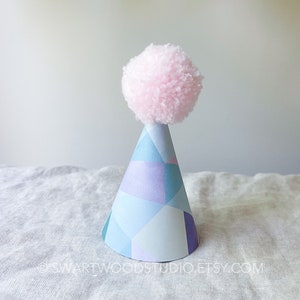 May include: A blue and purple geometric patterned party hat with a pink pom-pom on top.