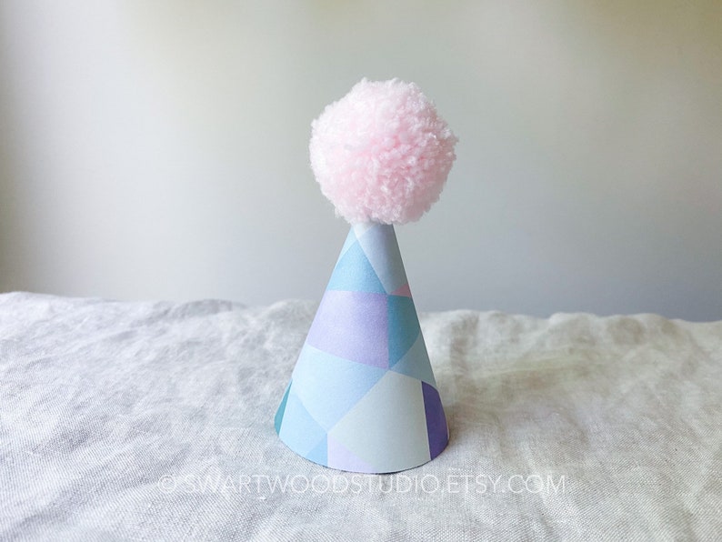 May include: A blue and purple geometric patterned party hat with a pink pom-pom on top.