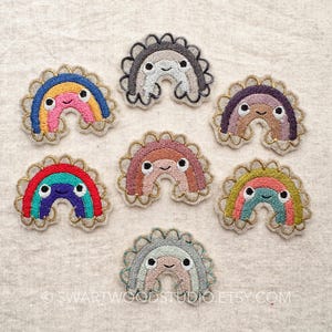 May include: Set of 8 embroidered rainbow patches with smiling faces. Each rainbow is a different color and has a scalloped edge.