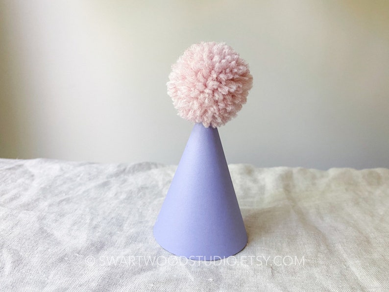 May include: A lavender party hat with a pink pom-pom on top.