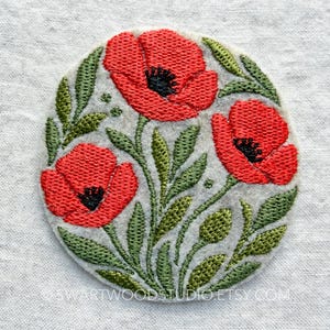 May include: A circular embroidered patch featuring three vibrant red poppy flowers with black centers and detailed green stems and leaves on a light beige felt background. The text SWARTWOODSTUDIO.ETSY.COM is printed in small white letters at the bottom.