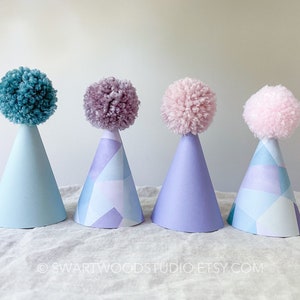 May include: Four party hats with colorful pom poms on top. The hats are blue, purple, and pink with a geometric pattern.