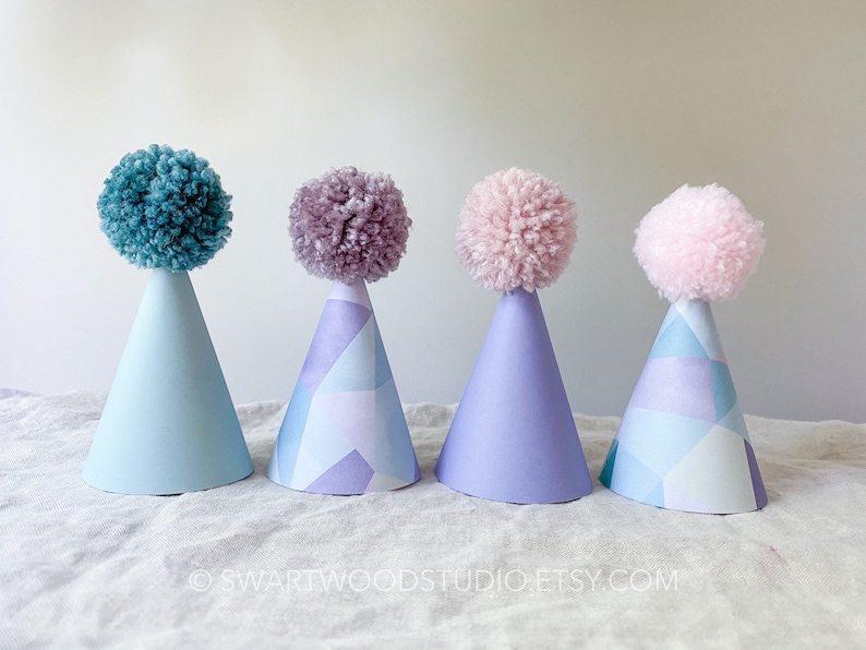 May include: Four party hats with colorful pom poms on top. The hats are blue, purple, and pink with a geometric pattern.