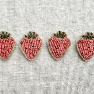 May include: Four pink felt strawberry appliques with green felt leaves. The strawberries are embroidered with a textured pattern.