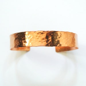 May include: A hammered copper bracelet with a smooth, rounded finish. The bracelet is made of a single piece of copper that has been hammered to create a textured surface.