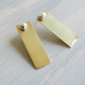 May include: A pair of gold rectangle earrings with a silver textured ball at the top of each earring.
