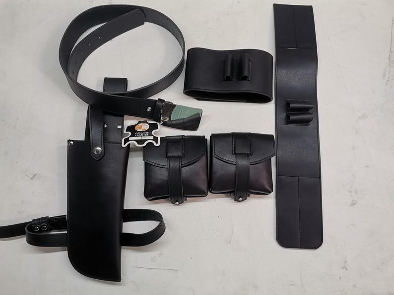 May include: A black leather belt with multiple pouches and a holster. The belt has a buckle and is decorated with a small leather tag that says "Genuine Leather".