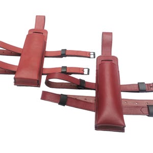 Peut inclure: Deux étuis en cuir rouge avec des sangles réglables. Les étuis sont conçus pour être portés sur la jambe et ont une fermeture à boucle.