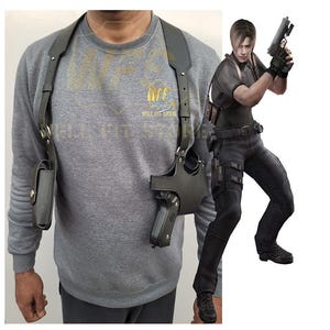 Könnte beinhalten: Ein schwarzes Leder-Schulterholster mit einer Pistole und einem Magazin-Fach. Das Holster wird über einem grauen Sweatshirt getragen. Der Text "WELL FIT STORE" ist auf dem Sweatshirt sichtbar.