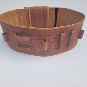 May include: A brown leather tool belt with multiple pockets and loops. The belt has a brown leather strap with a black buckle.