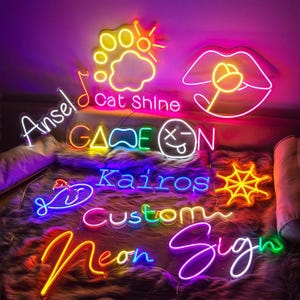 May include: A collection of colorful neon signs, including the words "Ansel", "Cat Shine", "Game On", "Kairos", "Custom", and "Neon Sign". The signs feature various shapes like lips, a sun, a musical note, and a fish. The signs are lit in yellow, pink, blue, and green.