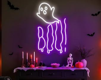May include: A neon sign in the shape of a ghost with the word "BOO" in purple. The sign is mounted on a dark wall with black bat decorations. A table below has candles, a skeleton, and a pumpkin.