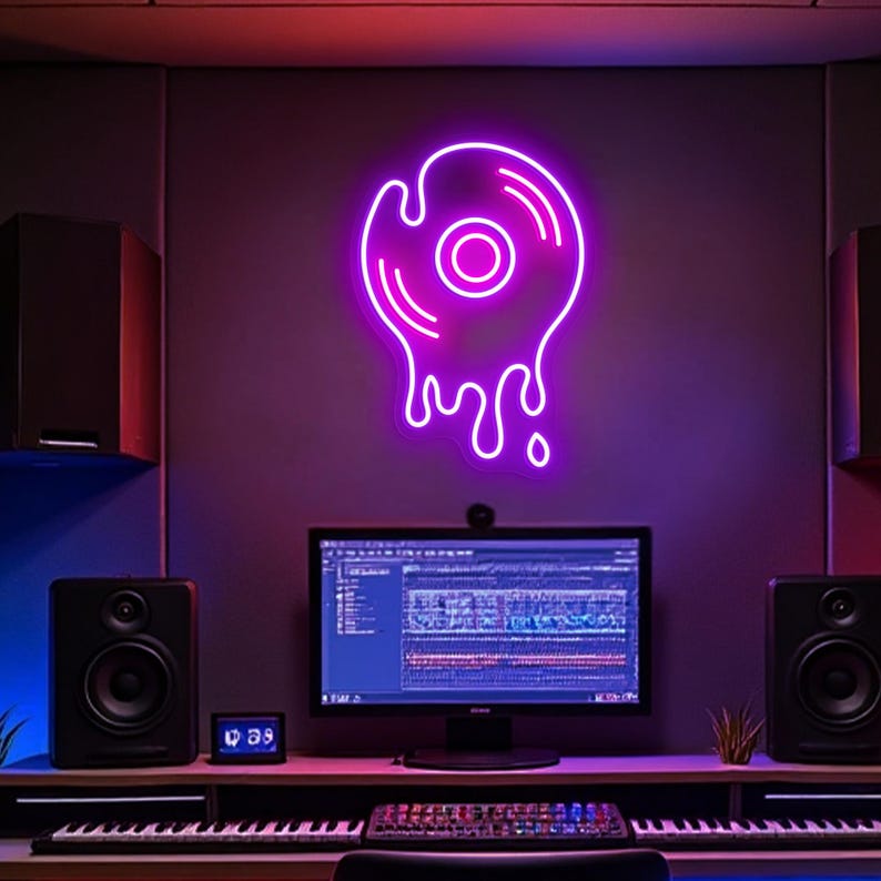 May include: A neon sign in the shape of a melting vinyl record glows purple against a gray wall. The sign is above a desk with a computer, speakers, and a keyboard. The room has a recording studio vibe.