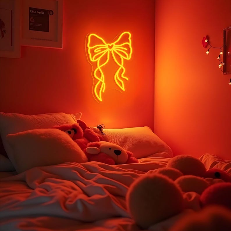 May include: A bedroom with a white bed and orange walls. The bed has a white comforter and several pillows. There is a neon yellow bow sign on the wall.