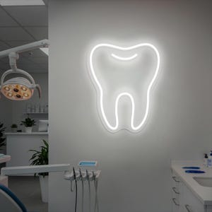 Puede incluir: Un letrero de neón blanco brillante con forma de molar cuelga de una pared blanca. El entorno del consultorio dental incluye una lámpara dental, instrumentos dentales y un lavabo.