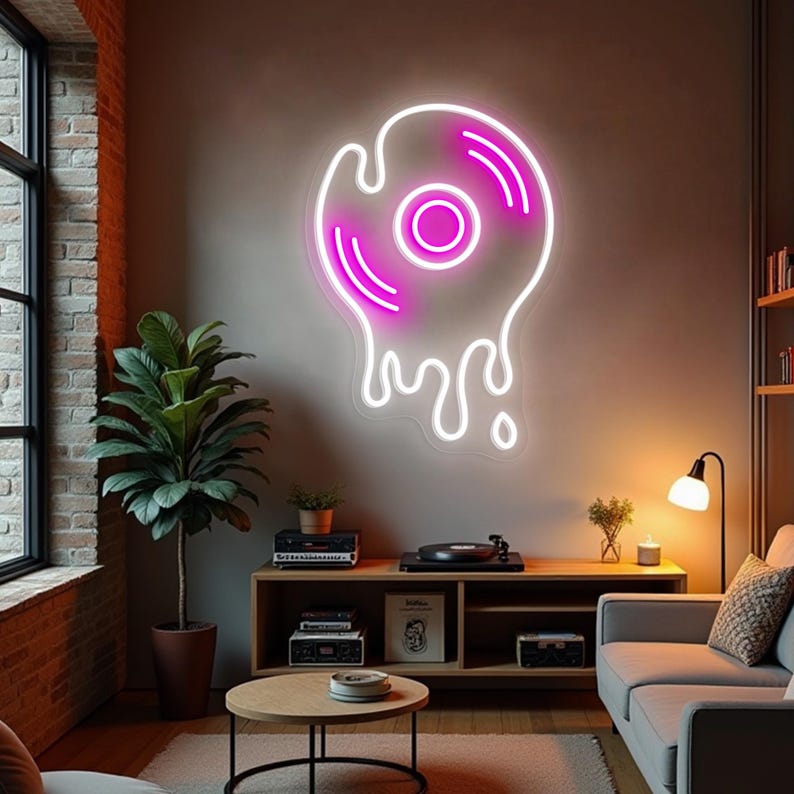 May include: A neon sign shaped like a melting vinyl record, with a white outline and a bright pink center and accents. The sign is mounted on a neutral-colored wall in a living room setting. The room includes a record player, a sofa, and a plant.