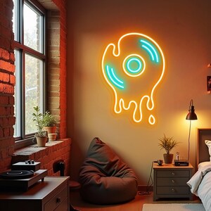 May include: A neon sign shaped like a melting vinyl record, with a bright orange outline and turquoise accents. The sign is mounted on a beige wall in a room with a brick wall, a window, and a beanbag chair.