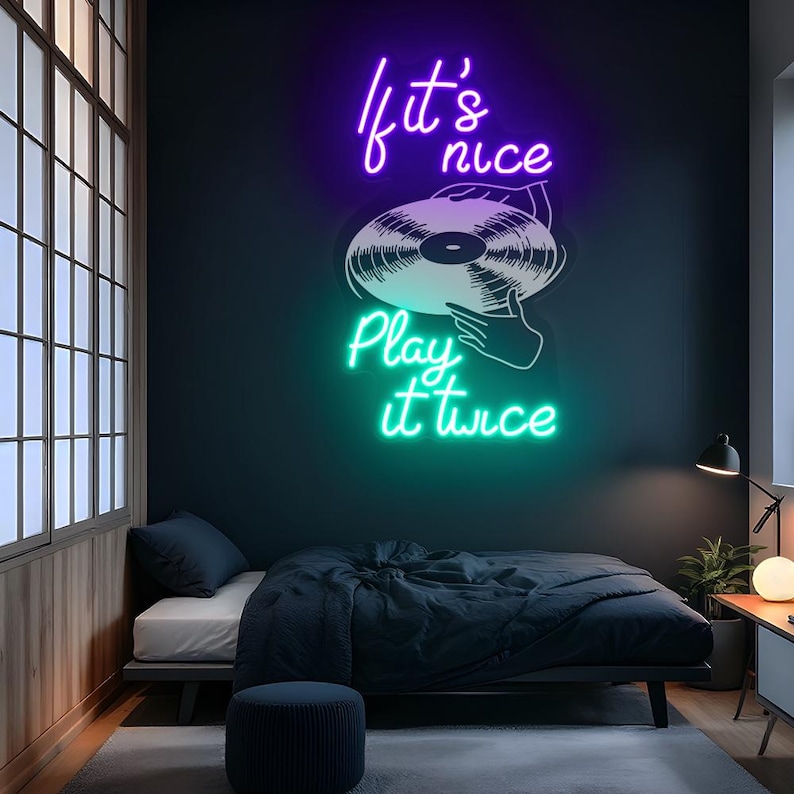 May include: A neon sign with the text "If it's nice, play it twice" in purple and green. The sign features a graphic of a vinyl record and hands. The sign is mounted on a dark blue wall above a bed.