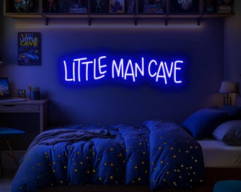 Op de afbeelding: Een slaapkamer met een blauw neonbord met de tekst "LITTLE MAN CAVE". De kamer heeft een bed met een blauw dekbedovertrek en een geel sterrenpatroon, een bureau en planken met decoratieve items. De muren zijn donkerblauw geschilderd.