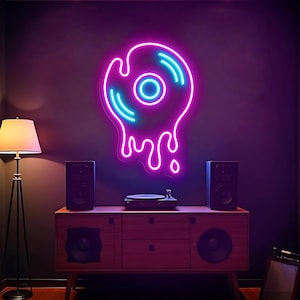 May include: A neon sign shaped like a melting vinyl record, with a pink outline and blue accents, hangs on a dark wall. A wooden cabinet with speakers and a record player sits below. A floor lamp is to the left.