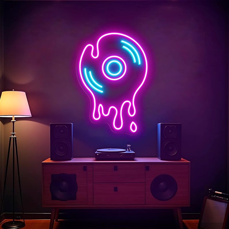 May include: A neon sign shaped like a melting vinyl record, with a pink outline and blue accents, hangs on a dark wall. A wooden cabinet with speakers and a record player sits below. A floor lamp is to the left.