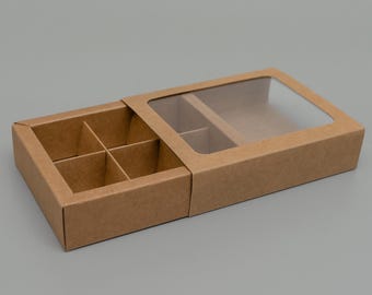 May include: A brown cardboard box with a clear plastic window on top. The box is divided into six compartments and is open to reveal the compartments.