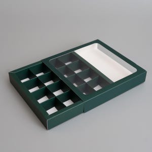 Peut inclure: Une boîte en carton vert foncé avec un couvercle en plastique transparent. La boîte est divisée en 16 compartiments pour contenir de petits objets, tels que des chocolats ou des bijoux.