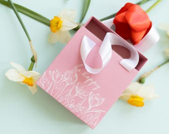 Caja de regalo rosa con estampado floral, asa con cinta "Be Happy" y caja deslizante de cartón.