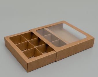 May include: A brown cardboard box with a clear plastic lid. The box has nine compartments and is designed for packaging small items.