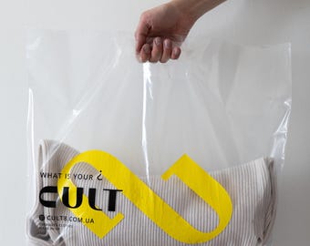 Könnte beinhalten: Eine durchsichtige Plastiktüte mit einem weißen gerippten Shirt darin. Die Tüte hat ein gelbes Logo mit dem Schriftzug "WHAT IS YOUR CULT" und "CULT8.COM.UA", wobei das Wort "CULT" in Schwarz gehalten ist.