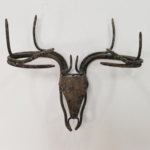 Puede incluir: Una escultura de cabeza de ciervo de metal con un acabado marrón rústico. Las astas están hechas de metal retorcido y la cabeza es una pieza sólida de metal.