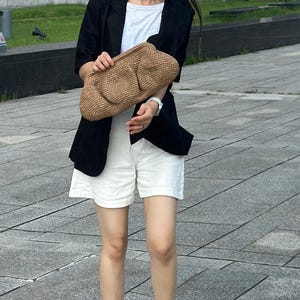 May include: A woman wearing a black blazer, white shorts, and white sneakers with black stripes. She is holding a brown woven bag.