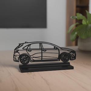 Peut inclure: Une sculpture de voiture noire stylisée. La voiture est représentée en contour linéaire, avec des roues et des fenêtres détaillées. Elle repose sur une base rectangulaire, créant une esthétique moderne et minimaliste. La sculpture est probablement en matériau solide.
