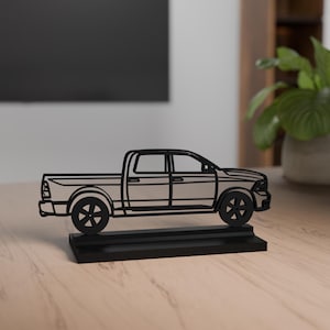 Op de afbeelding: Een zwart metalen draadsculptuur van een pick-up truck silhouet, met een gedetailleerde omtrek van de carrosserie, wielen en ramen, gemonteerd op een stevige rechthoekige zwarte basis voor stabiliteit en weergavedoeleinden.