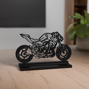 Op de afbeelding: Zwarte motorfiets sculptuur met ingewikkelde uitgesneden details, gemonteerd op een rechthoekige basis. De sculptuur toont een gedetailleerd motorfietsontwerp, met wielen, motor en carrosserie. Een decoratief item voor motorliefhebbers.
