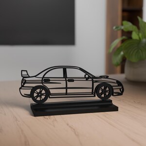 Könnte beinhalten: Schwarze Metall-Autoskulptur mit Spoiler und detaillierten Rädern, montiert auf einem rechteckigen Sockel. Das Auto ist ein dekoratives Objekt, geeignet für einen Schreibtisch oder ein Regal.