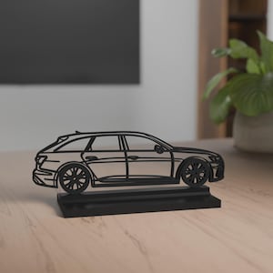 Könnte beinhalten: Eine schwarze, stilisierte Autoskulptur. Das Auto ist ein Kombi-Design mit detaillierten Rädern und Karosserielinien. Es steht auf einem rechteckigen Sockel, alles in Schwarz. Die Skulptur steht auf einer hellen Holzoberfläche.