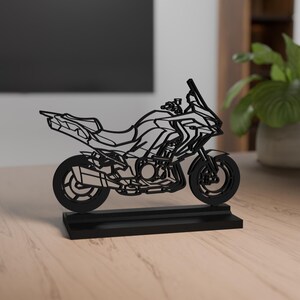 Può includere: Scultura di motocicletta nera con design dettagliato, montata su una base rettangolare. La motocicletta presenta un parabrezza, componenti del motore e ruote a raggi. La scultura è esposta su una superficie di legno.
