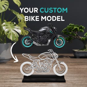 May include: A custom bike model display featuring a dark grey motorcycle with bright teal wheels positioned above a white wireframe outline of the same motorcycle on a black rectangular base, with the text YOUR CUSTOM BIKE MODEL above.