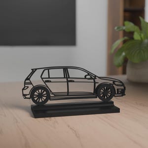 Könnte beinhalten: Eine schwarze Autoskulptur im Fließheck-Stil. Die Räder und Fenster sind detailliert. Das Auto steht auf einem rechteckigen schwarzen Sockel und bietet ein modernes, minimalistisches Design.
