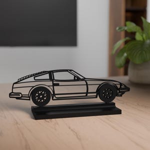 Könnte beinhalten: Schwarze Metall-Autoskulptur auf schwarzem Sockel. Das Auto hat ein klassisches Sportwagendesign mit detaillierten Rädern und einem schlanken Profil. Die Skulptur wird auf einer Holzoberfläche ausgestellt.
