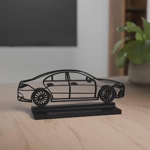 May include: A black and silver car sculpture. The car is a sedan with detailed wheels and a sleek design. It is mounted on a black rectangular base, suitable for display on a desk or shelf.