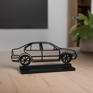 Può includere: Una scultura di auto in metallo nero con carrozzeria colorata e ruote nere. L'auto è in stile berlina e poggia su una base rettangolare nera. La scultura è esposta su una superficie di legno.